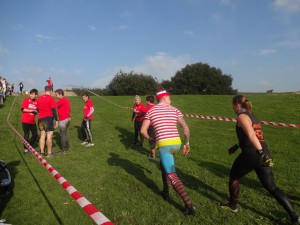 A team in red and a Wally from the "Where's Wally" books heading up a hill